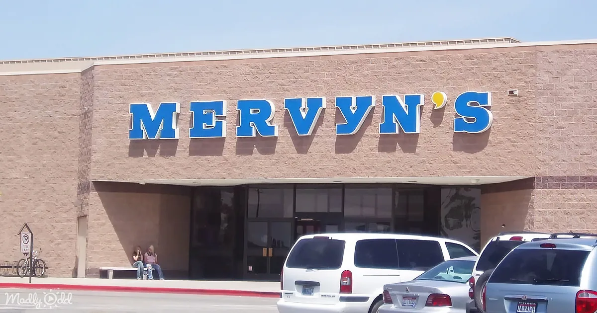 Mervyn's store sign is prominently displayed on a brick facade with parked cars and people sitting outside.