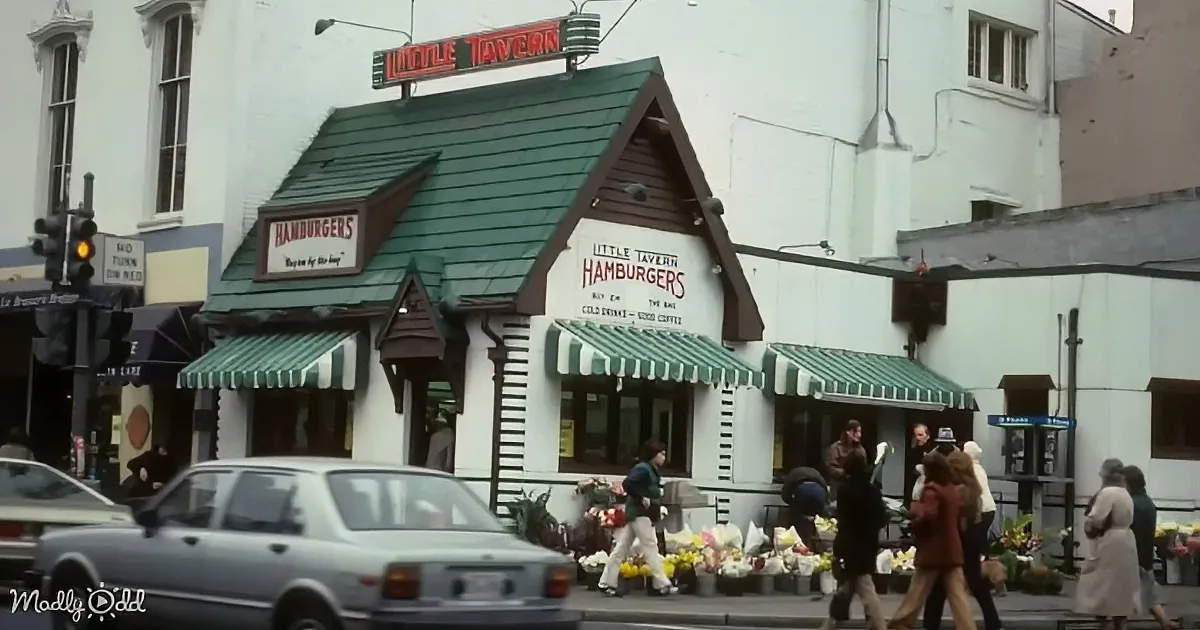 A small, quaint Little Tavern Hamburgers restaurant with green awnings and a sign, bustling with people and flowers on...