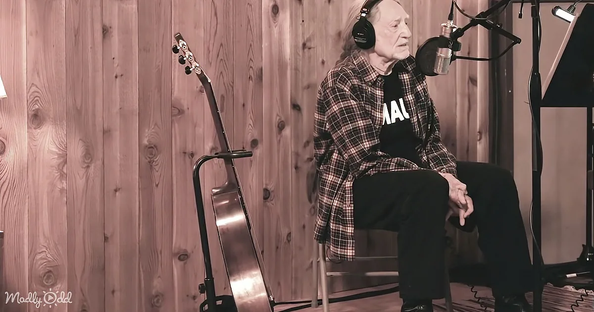 An elderly person wearing headphones sits in a chair, surrounded by musical equipment, in a wooden-paneled room.