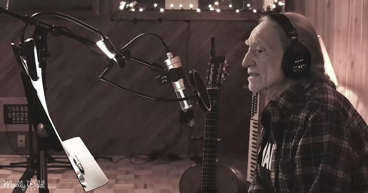 An older man wearing headphones sings into a microphone in a cozy recording studio.