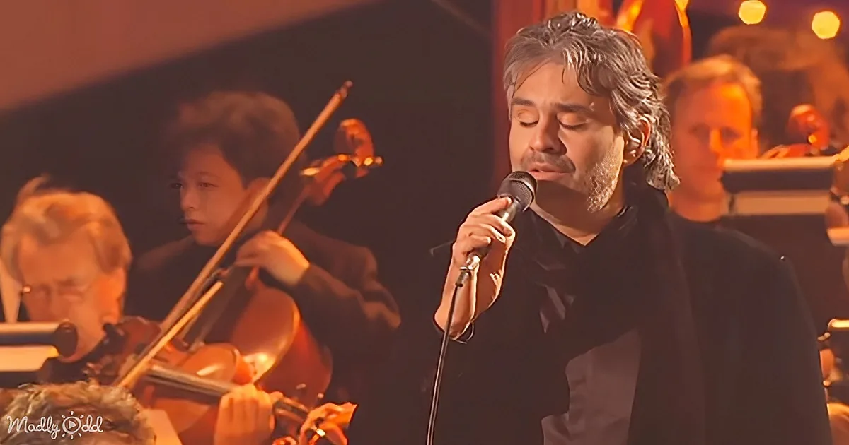 A man in black sings into a microphone, surrounded by musicians playing instruments.
