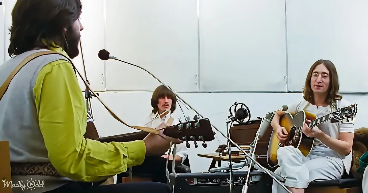 A man in a yellow shirt plays guitar, singing into a microphone, with two others in the background.