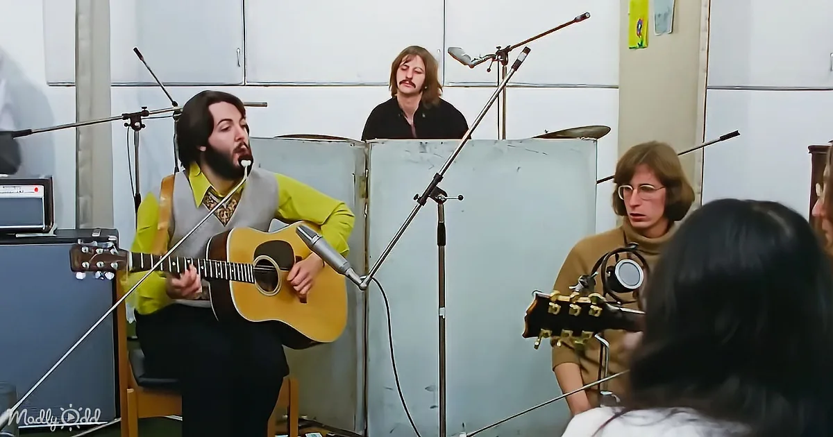 A man in a yellow shirt plays guitar in a recording studio with microphones and other musicians.