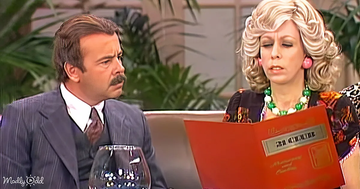 A man in a suit holds a wine glass while a woman in a colorful dress reads a menu.