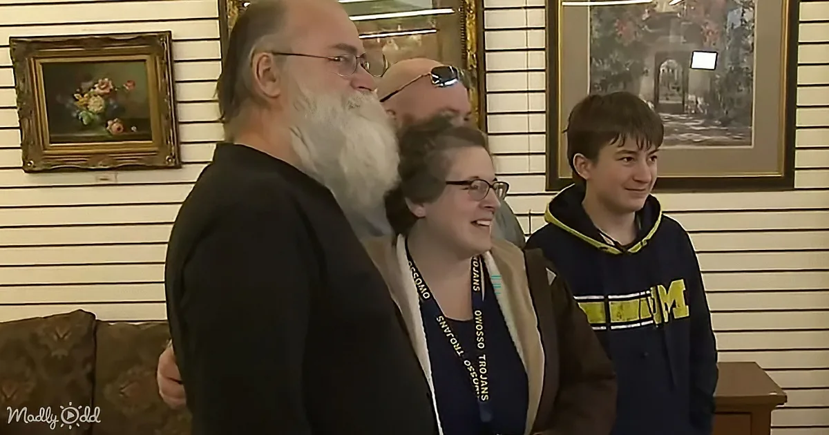 A man with a long white beard stands in a room with two women and a boy, all smiling.