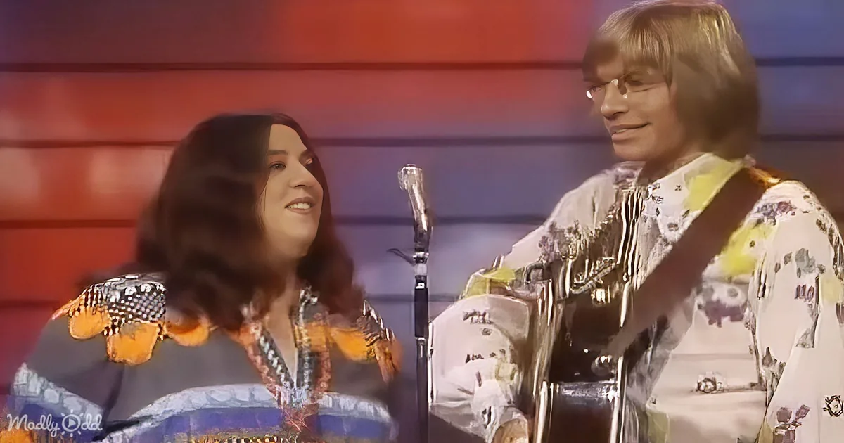 A man and woman in colorful, patterned outfits are performing on stage, smiling and holding microphones.