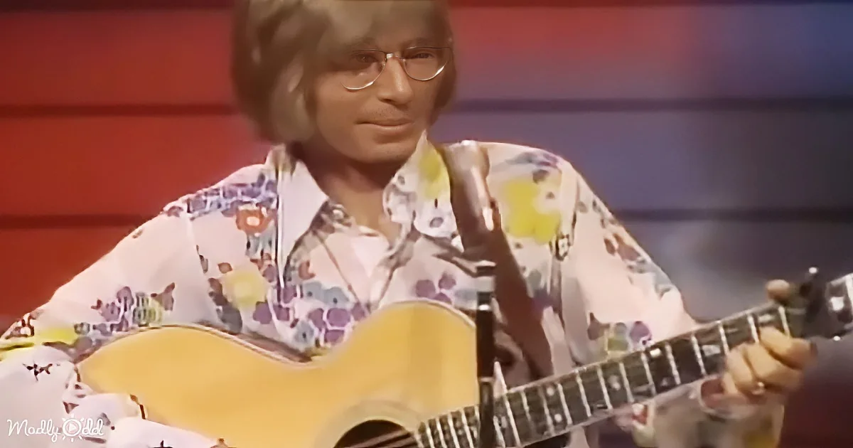 A person in a floral shirt plays an acoustic guitar on stage.