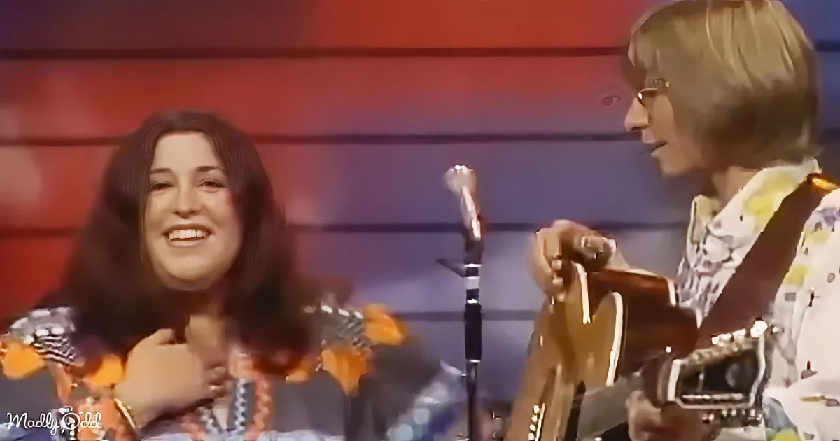 A woman in a colorful outfit smiles while holding a guitar, with another person in a patterned shirt nearby.