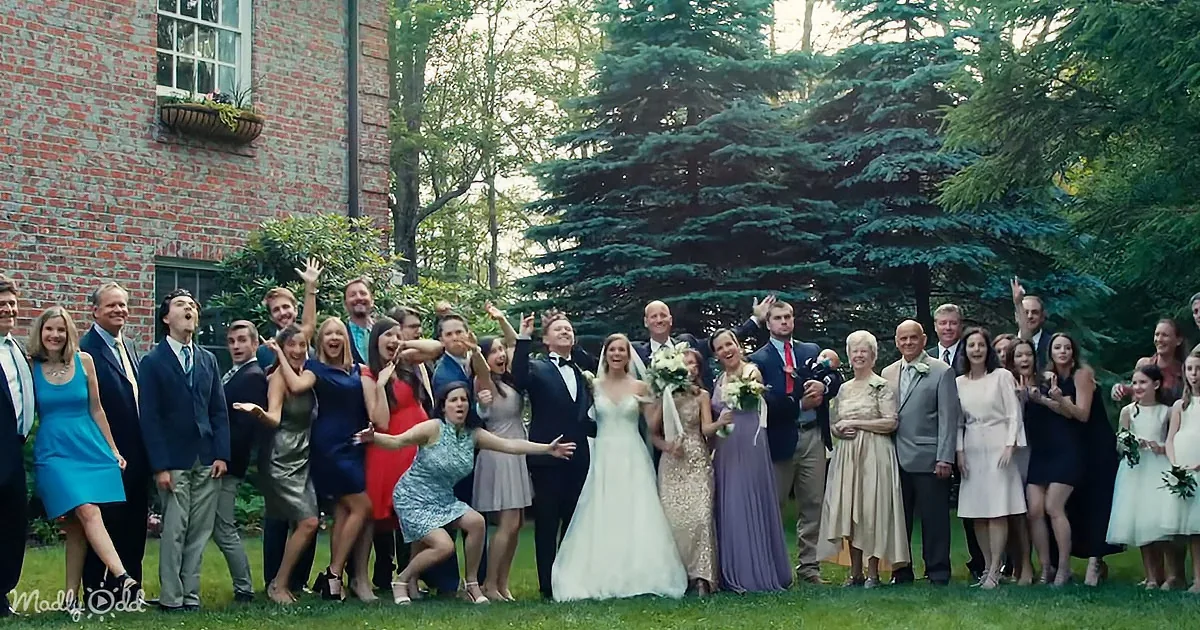 A bride in a white dress stands with her arms around her groom in a tuxedo, surrounded by a joyful group of family and...