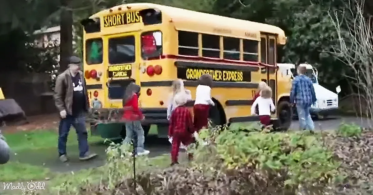 A yellow school bus labeled "Grandfather Express" is surrounded by people and children near a forested area.