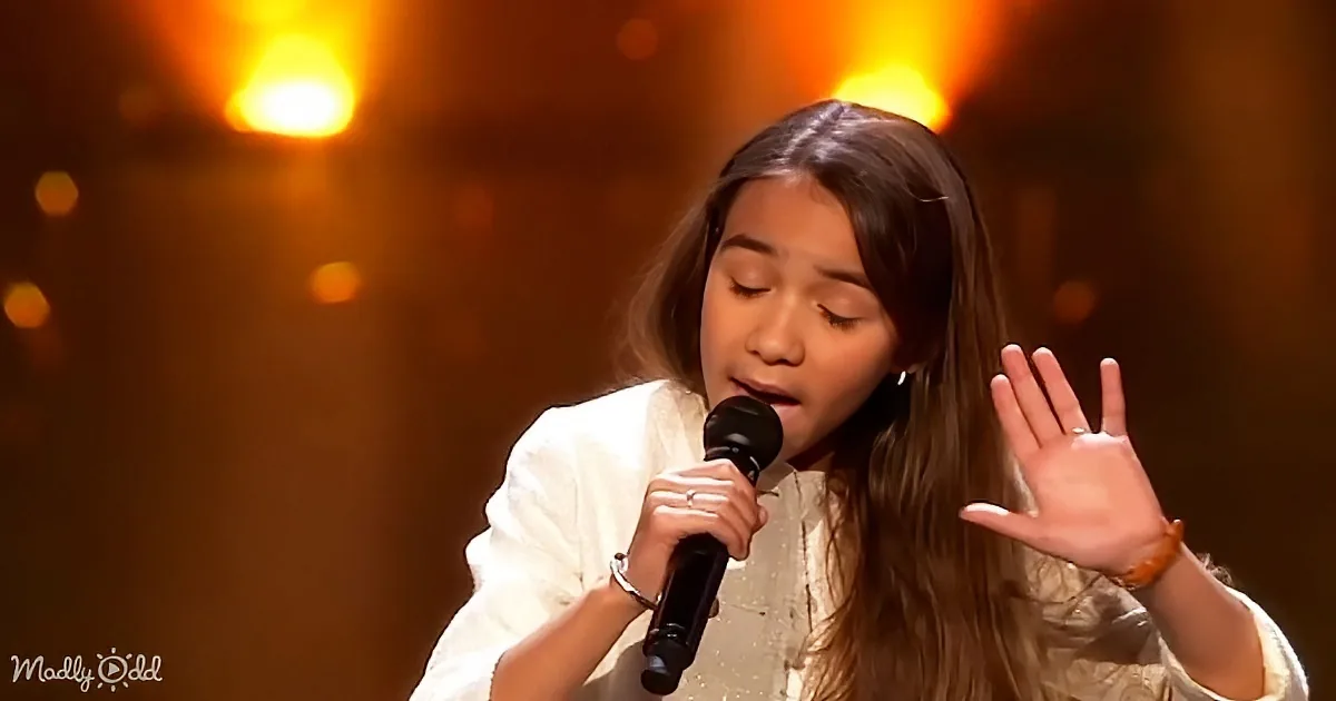 A person in white holds a microphone, singing with eyes closed, hand raised, against a warm, glowing background.