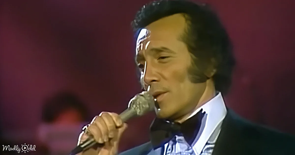 A man in a suit and bow tie sings into a microphone, holding it close to his mouth.