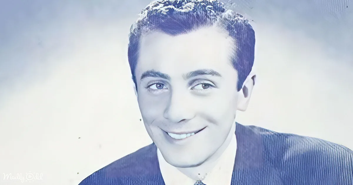 A smiling man with dark hair, wearing a blue corduroy jacket, against a light, textured background.