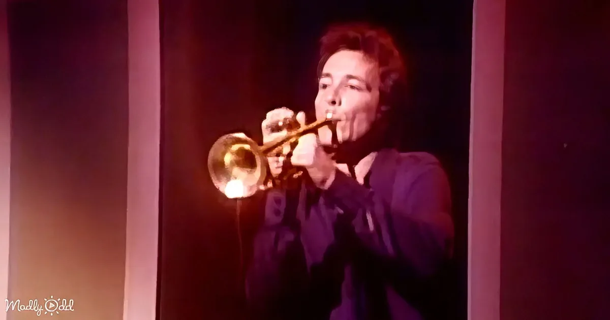 A person is playing a trumpet on stage with a purple and red lighting effect.