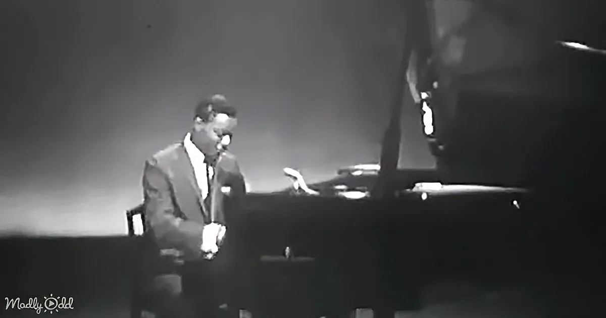 A man in a suit and hat plays piano on stage, singing into a microphone.