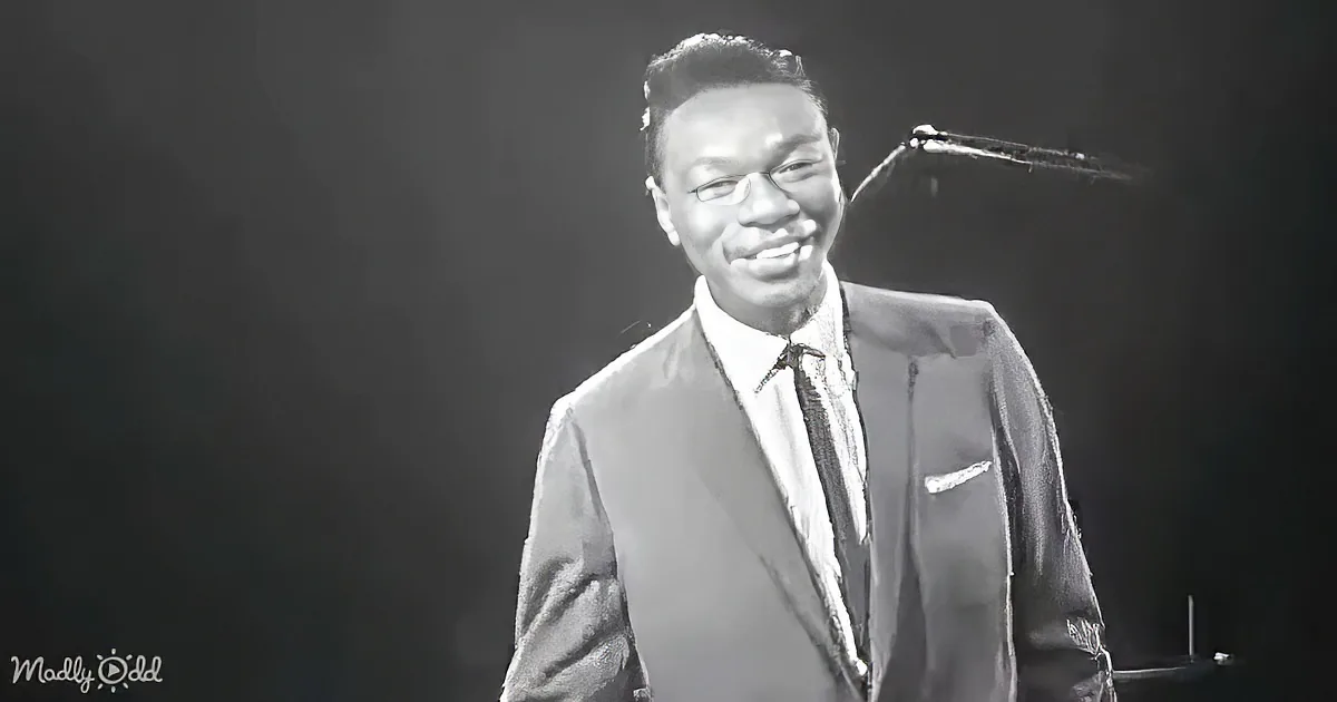 A man in a suit and tie smiles while playing a piano, with a microphone above him.