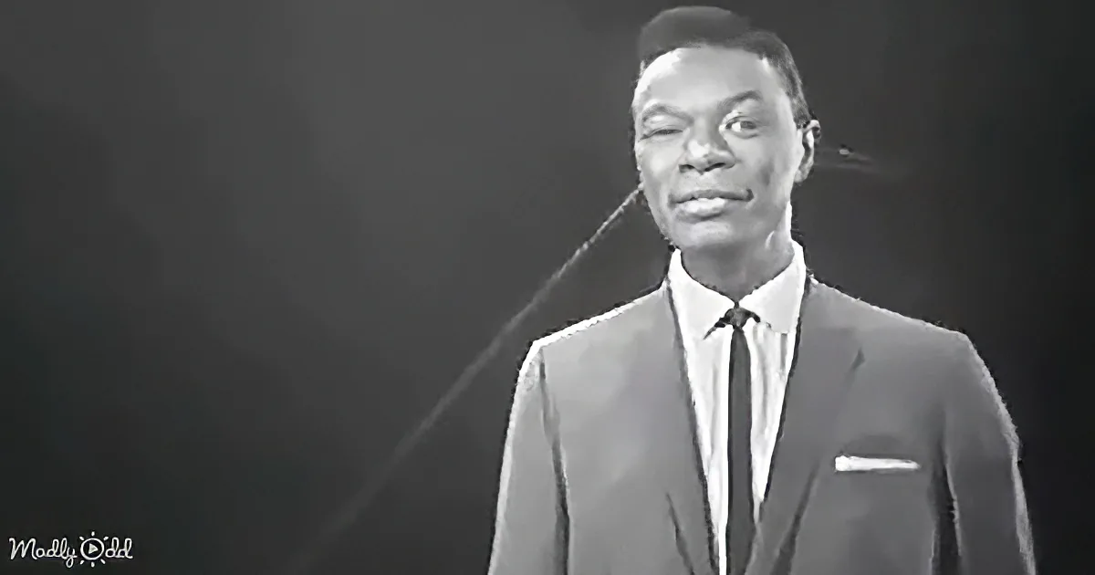 A man in a suit and tie smiles, wearing a hat, against a dark background.