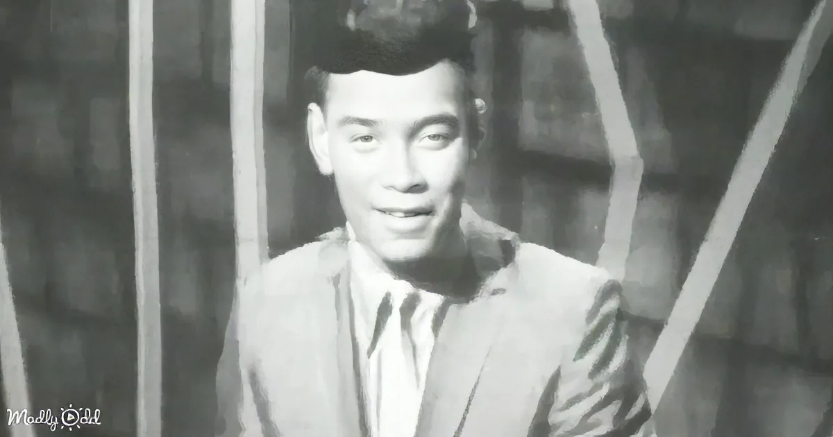 A man in a suit and tie, smiling, with a blurred background of bamboo.