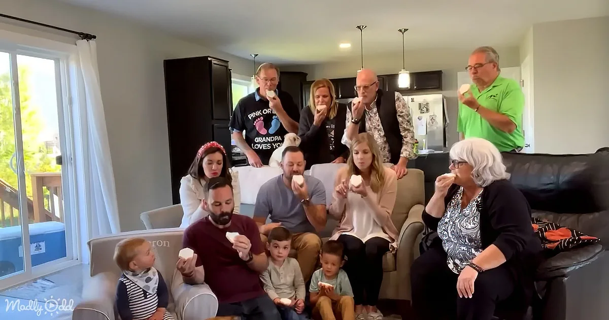 A family of 11 people, including adults and children, are gathered in a living room eating ice cream.