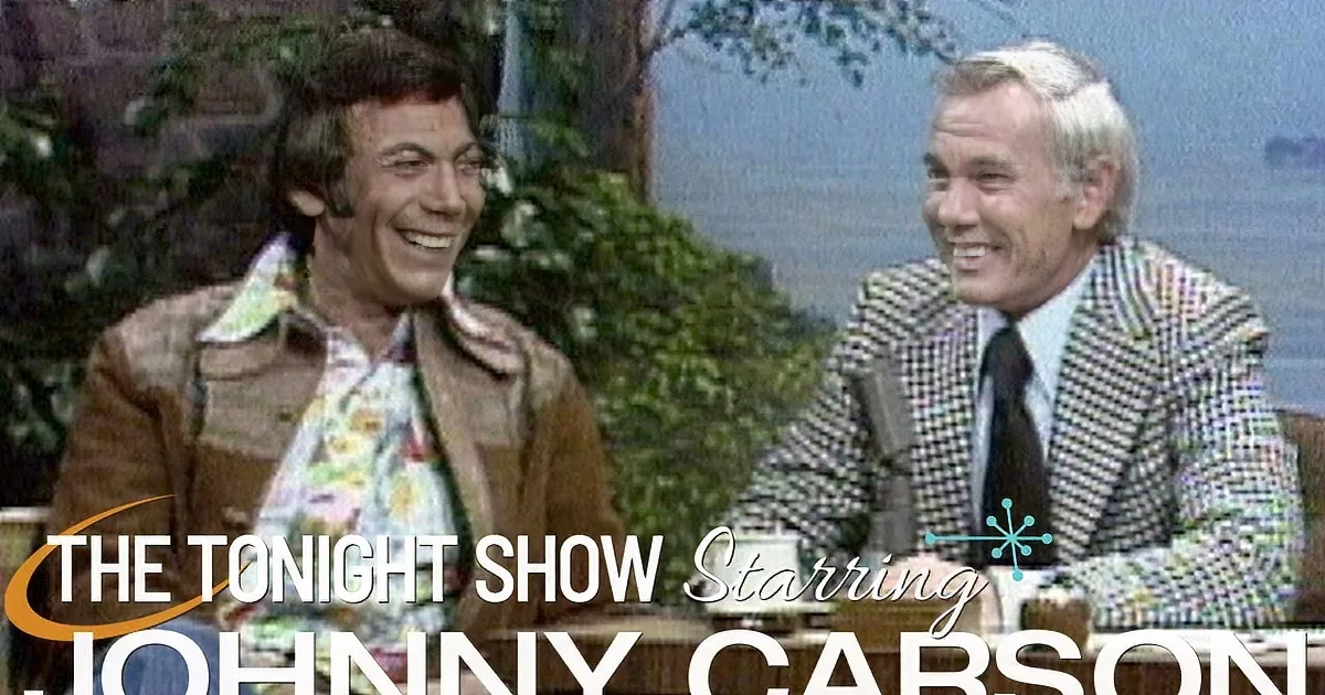 Two men in a studio setting, one in a colorful shirt and the other in a checkered suit, both smiling.
