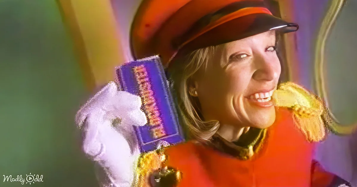 A person in a vibrant costume, holding a purple box, smiles brightly.
