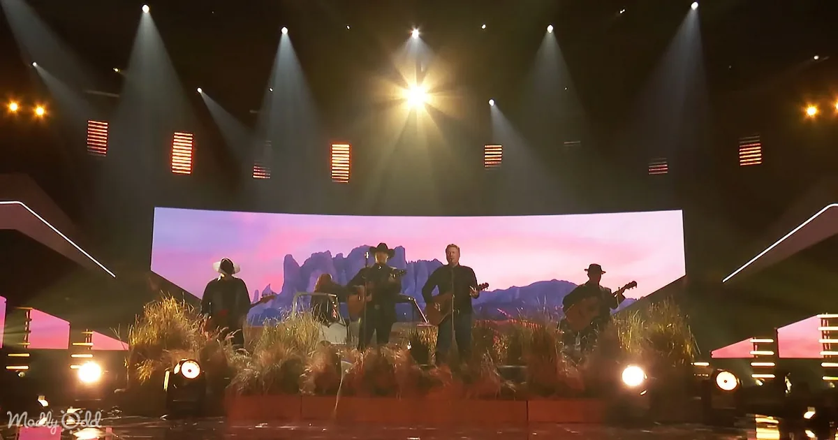 A band performs on stage with a desert backdrop and dramatic lighting.