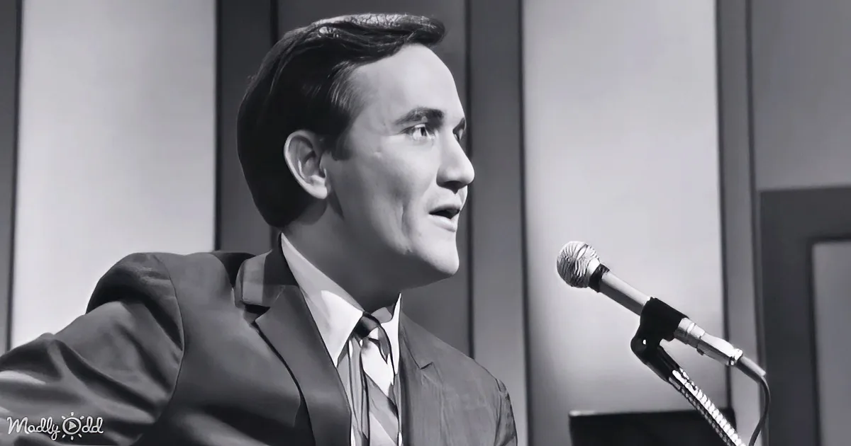 A man in a suit and tie is speaking into a microphone, looking to the side.