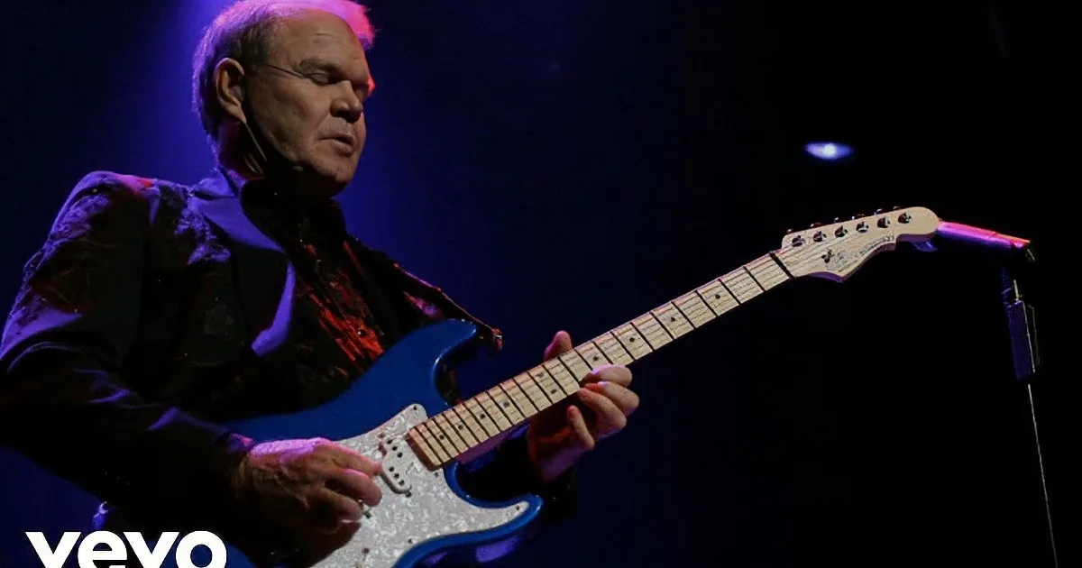 A man plays a blue electric guitar on stage under purple lighting.