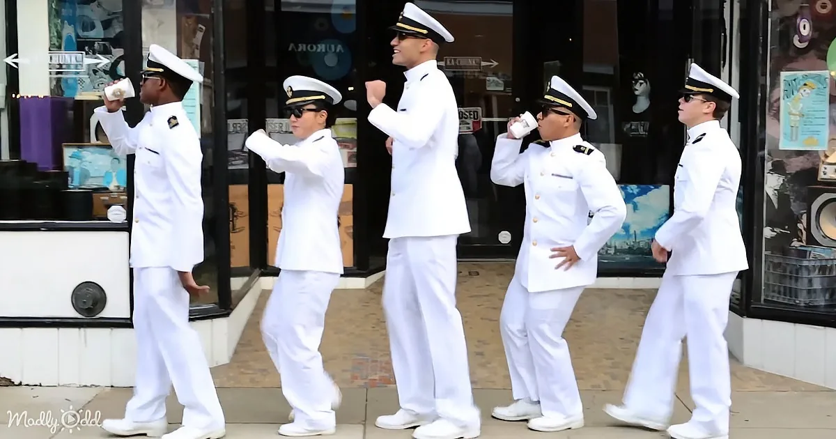 Five men in white uniforms and hats are dancing and drinking coffee outside a store.