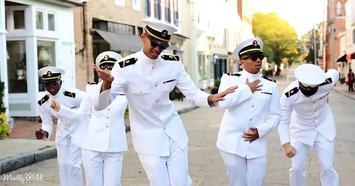 A group of people in white military uniforms is dancing on a street.