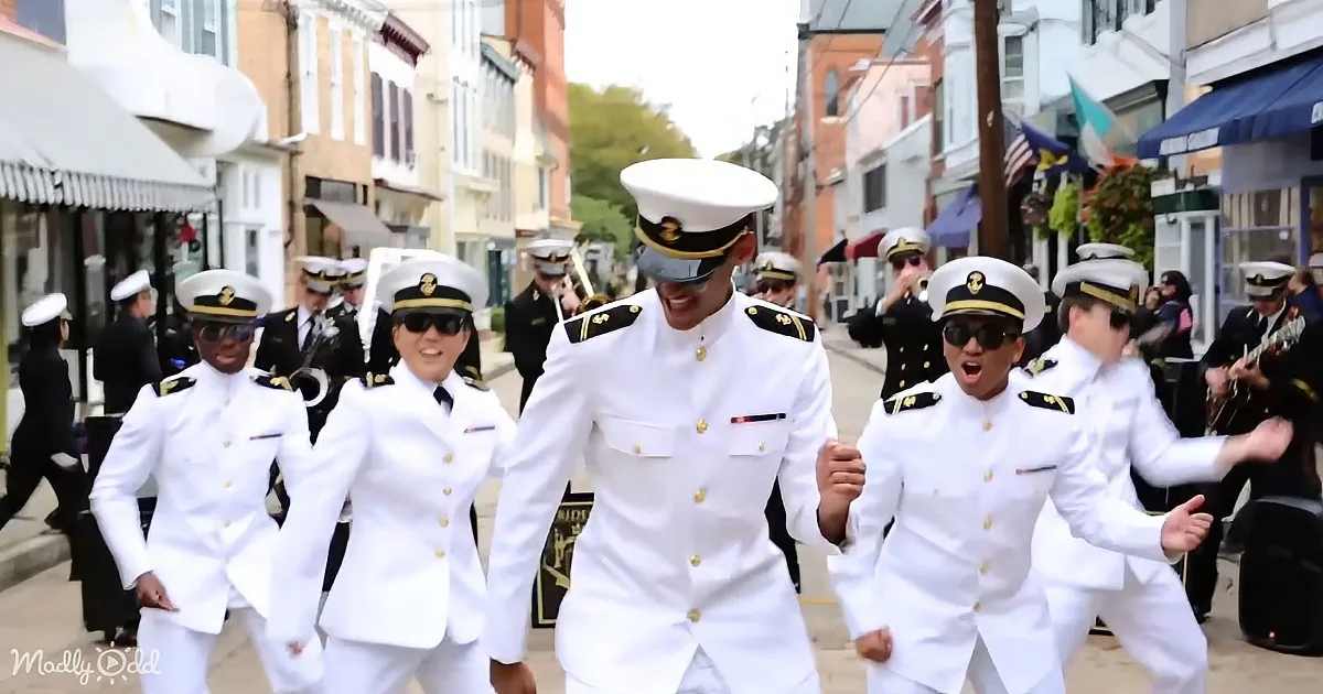A group of uniformed individuals in white military attire march down a street, smiling and enjoying themselves.