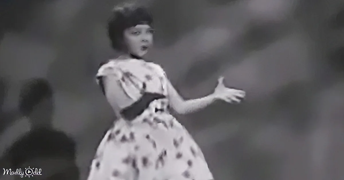 A woman in a floral dress sings with outstretched arms, captured in a black-and-white image.