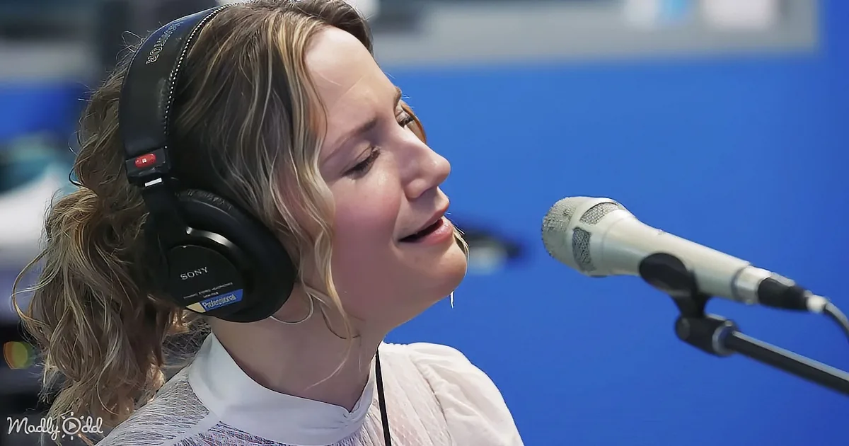 A woman wearing headphones sings into a microphone in a studio setting.