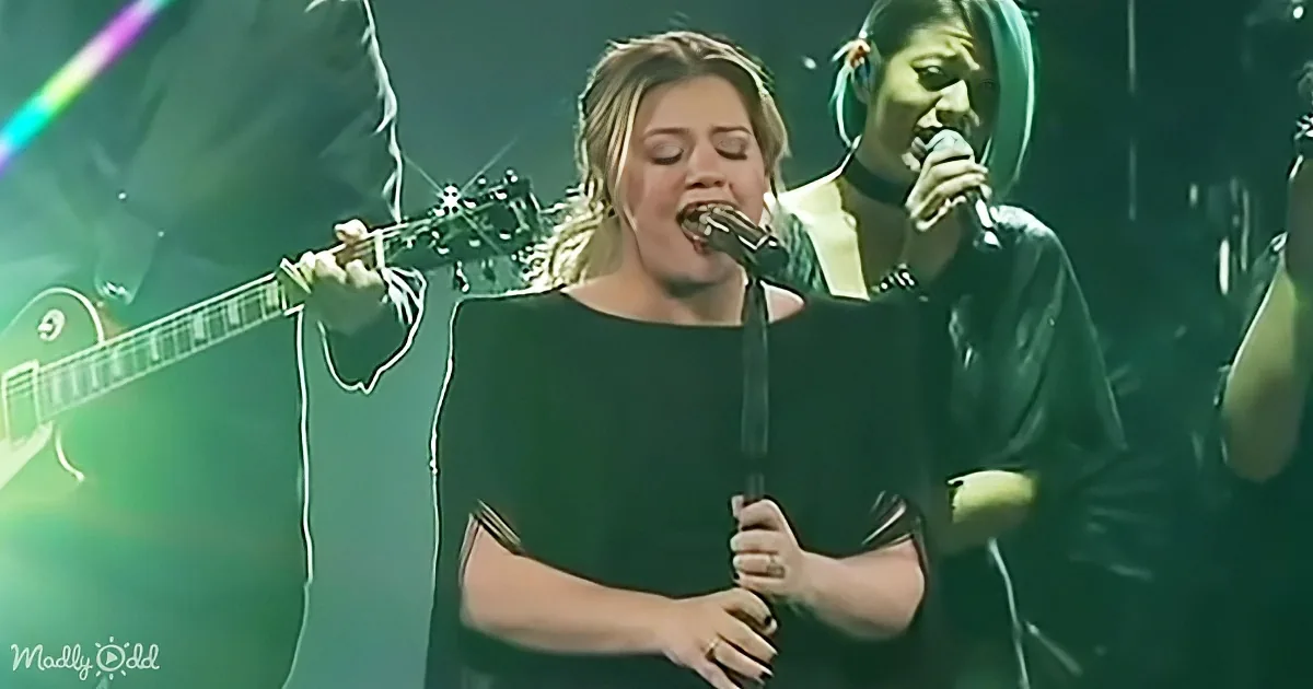 A woman in black sings passionately into a microphone on stage, surrounded by musicians and green lighting.