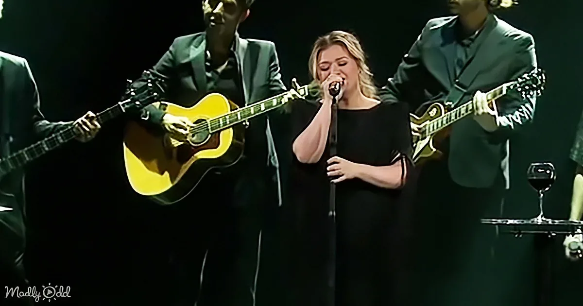 A woman sings passionately into a microphone, flanked by musicians playing guitars on stage.
