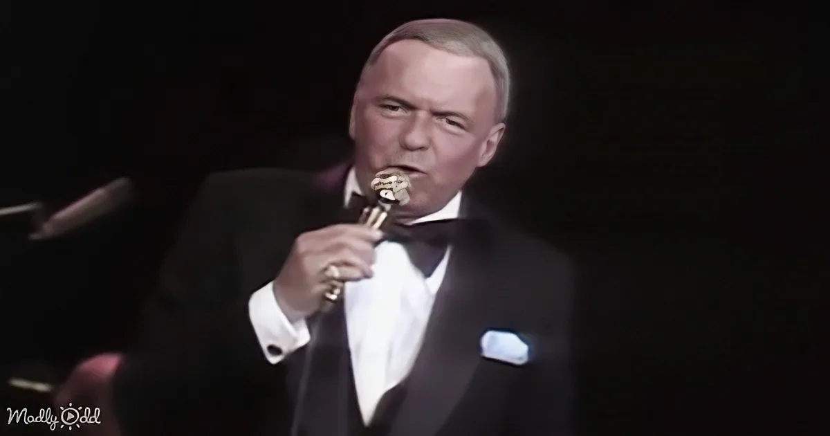 Frank Sinatra in a tuxedo sings into a microphone on stage.