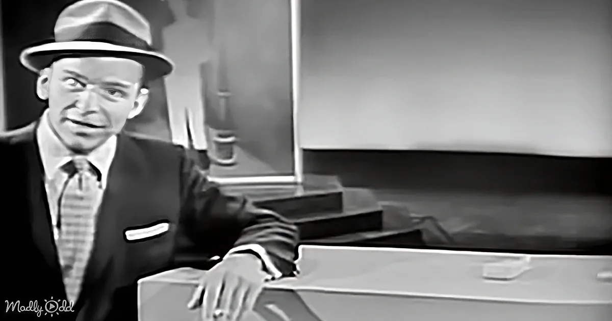 A man in a suit and hat is seated at a piano, appearing to play or sing.