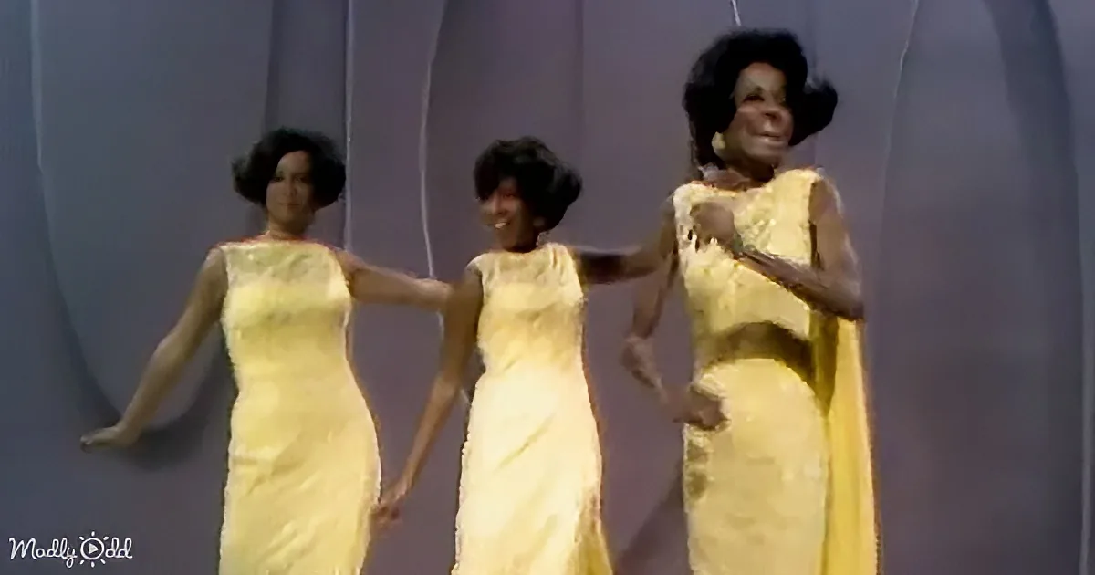 Three women in matching yellow dresses perform a synchronized dance on stage.