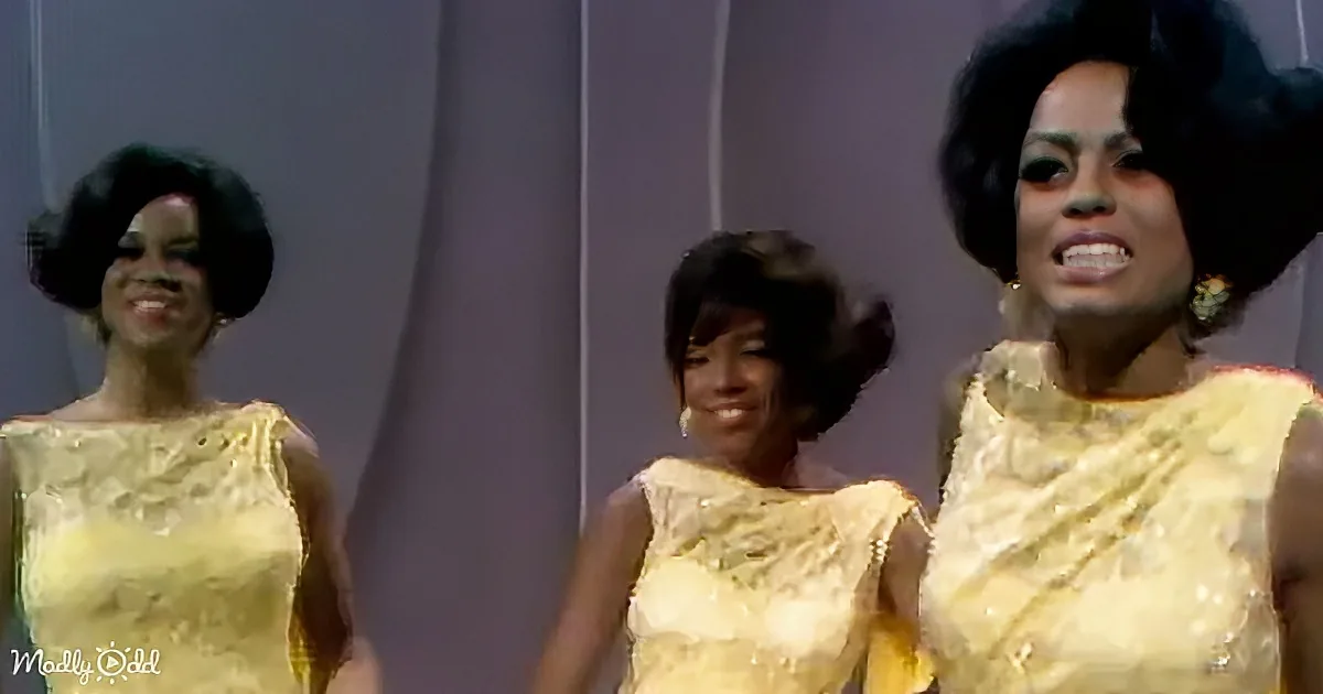 Three women in matching yellow dresses with afro hairstyles perform on stage.