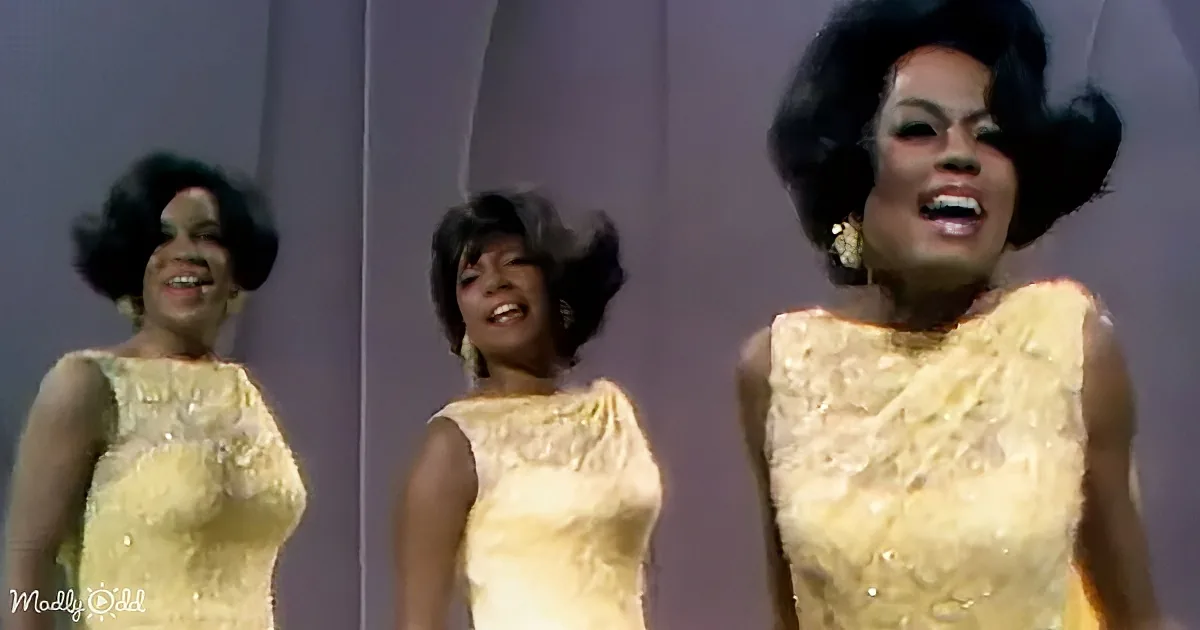 A woman in a yellow dress with a large afro hairstyle is singing on stage.