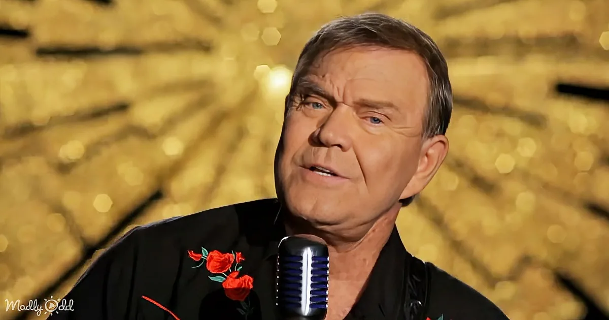 A man in a black shirt with red roses sings into a vintage microphone against a golden, bokeh background.
