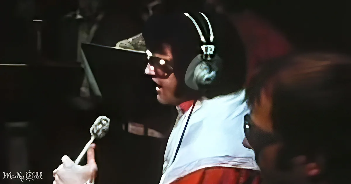 A person wearing headphones and a white shirt is holding a drumstick, likely playing drums.