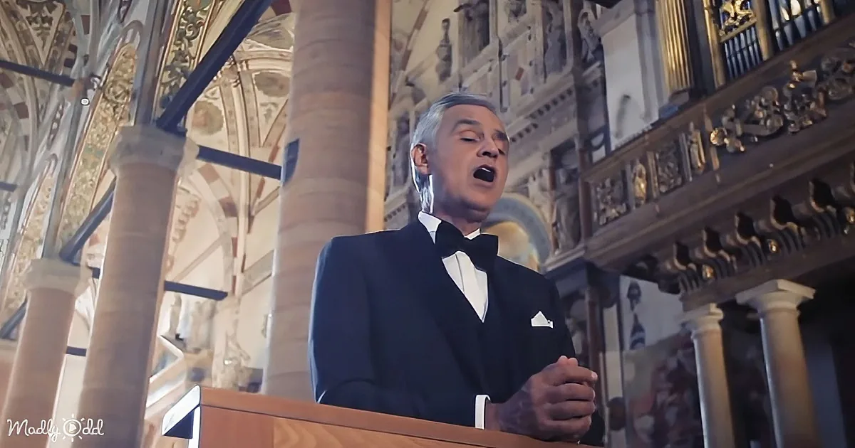 A man in a tuxedo sings passionately at a podium in a grand, ornate church setting.