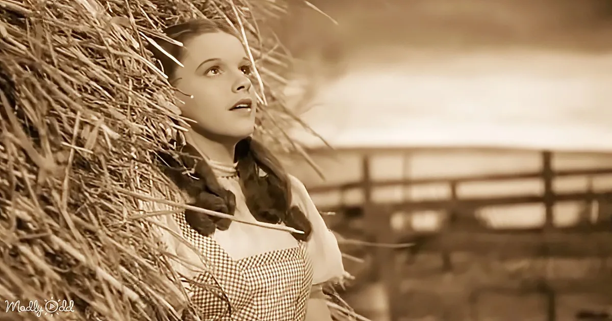A woman in a checkered dress leans against a hay bale, looking up with a serene expression.