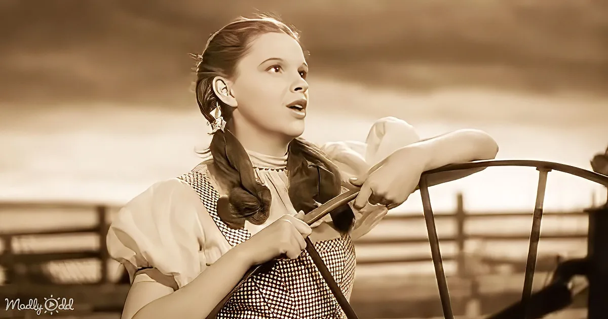 A woman in a vintage dress leans on a railing, holding a violin, against a sepia-toned backdrop.