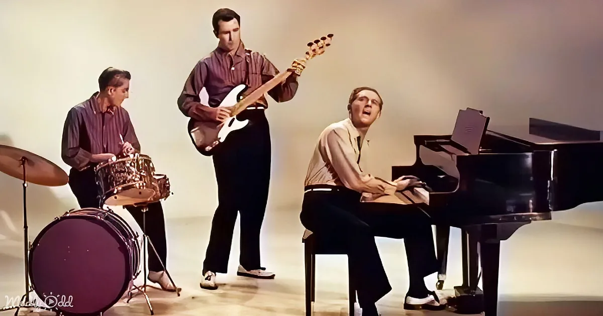 A man plays piano while another sings, a guitarist plays, and a drummer sets the rhythm.