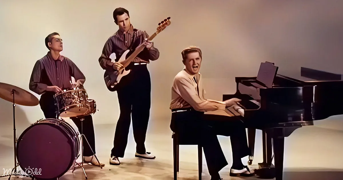 A man plays piano while another sings, a guitarist and drummer accompany in a musical performance.