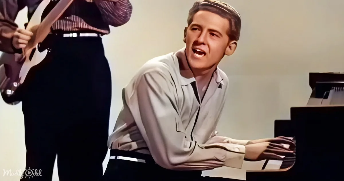 A man in a white shirt plays piano while another person plays guitar in the background.