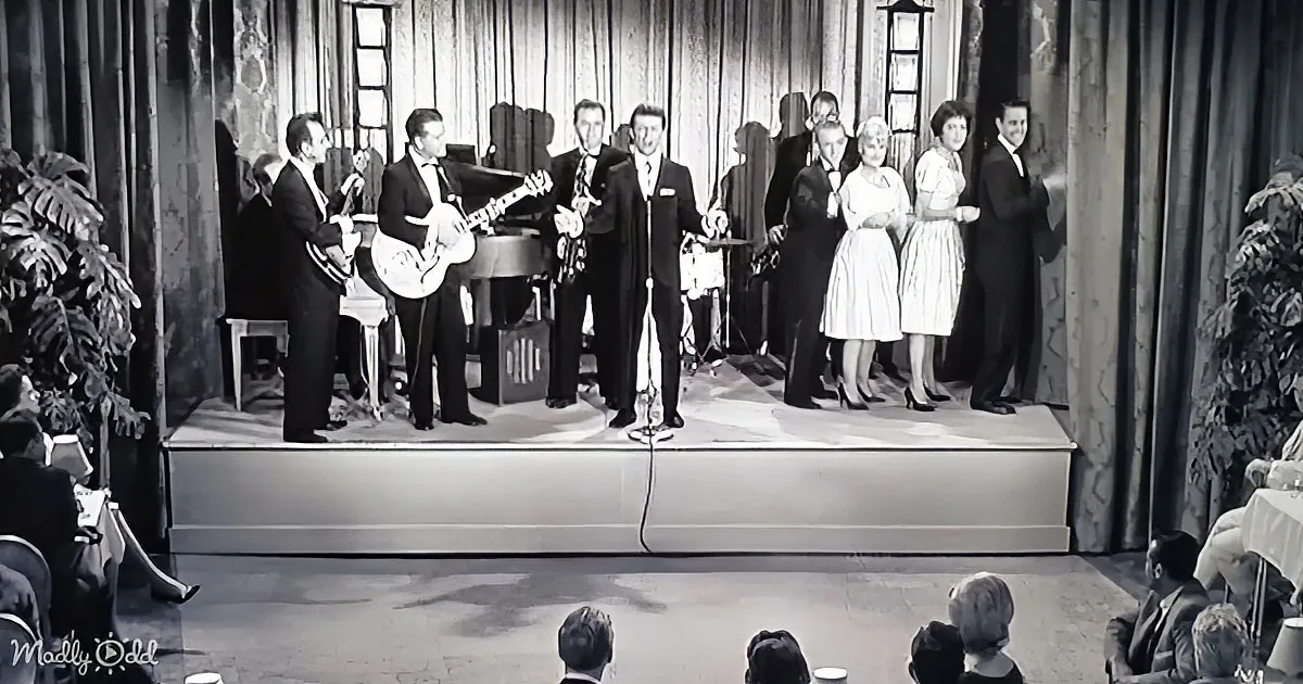 A band and singers perform on stage, with musicians playing instruments and a microphone in the foreground.