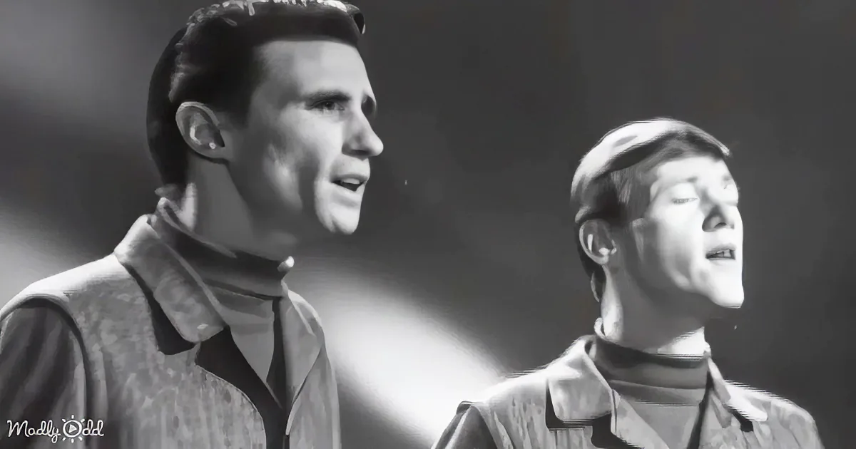 Two men in vintage clothing sing passionately, one with a patterned vest, the other in a turtleneck.